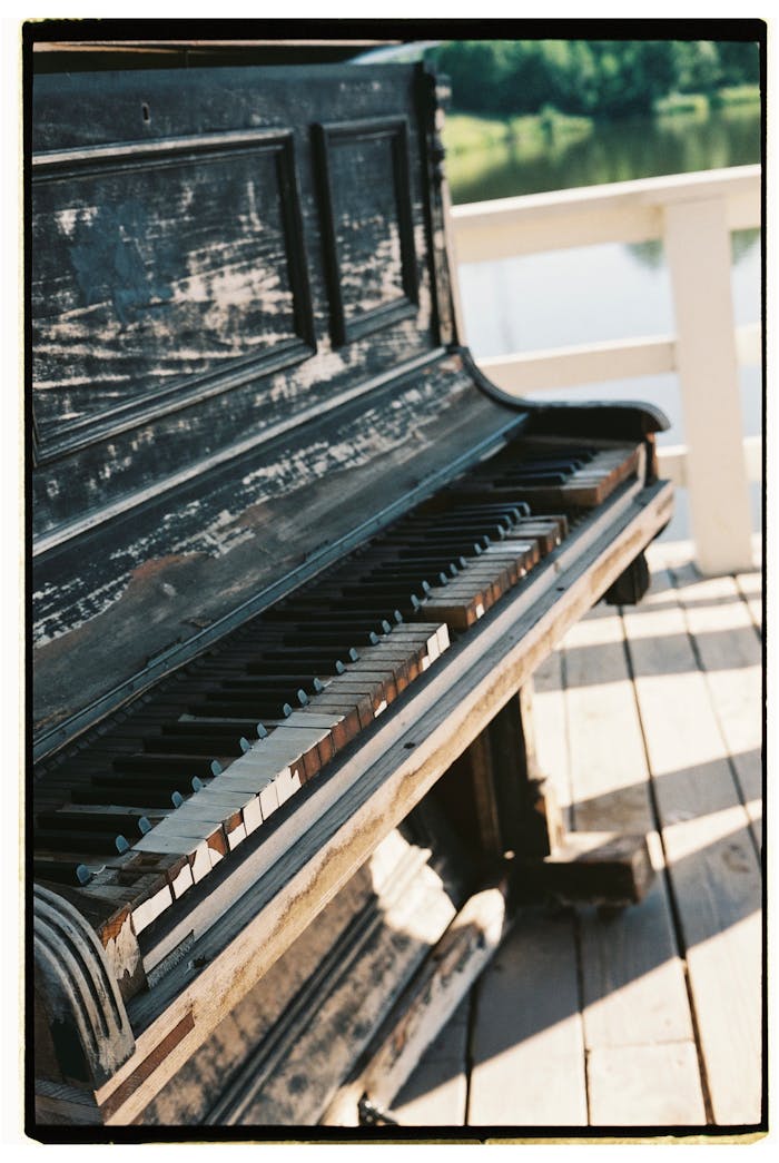 An old, weathered piano placed on a wooden pier by the water, showcasing decay and rustic beauty.